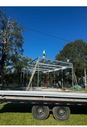 Crew installing a large metal frame structure with roofer on top